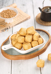 Golden Handmade Fried Tofu Puffs in Ceramic Dish with Soybeans on Rustic White Wood Background
