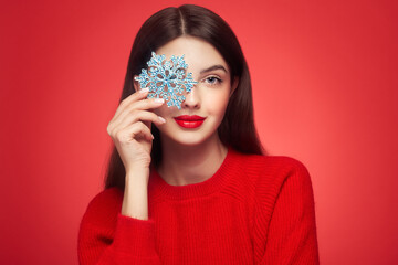 Beautiful young woman with red lipstick, shiny clean skin and face, showing glowing snowflake, near face and smiling, isolated on a red background. Christmas holidays concept