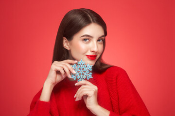Beautiful young woman with red lipstick, shiny clean skin and face, showing glowing snowflake, near face and smiling, isolated on a red background. Christmas holidays concept