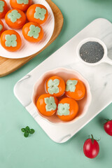 Fresh persimmon dumplings with decorative garnish on light mint background - Asian cuisine presentation