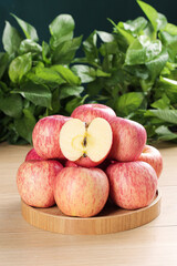 Fresh Red Fuji Apples on Wooden Plate with Sliced Apple and Green Leaves Background