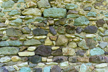 The masonry of an antique wall made of rough dark stones of different sizes and colors, bonded with light mortar. Some types of stones are cyan in color with a clear copper content.