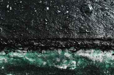 Close-up of a textured, dark surface with water droplets, contrasted by a light, iridescent, almost frozen lower section