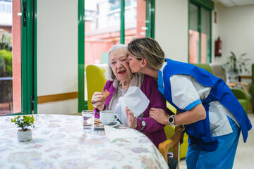 Caregiver kissing senior female resident during mealtime in a nursing home, providing compassionate care and support