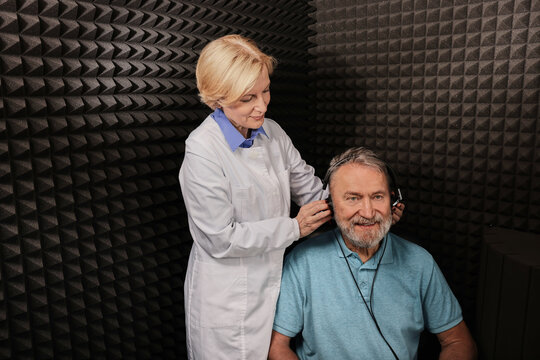 Audiometry. Audiologist doing hearing exam to a elderly man in soundproof audiometric cabin. Pure tone audiogram test