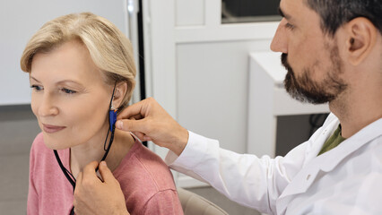 Audiologist carefully adjusts a hearing aid on a woman using advanced audiological equipment for personalized fitting
