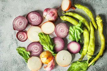 Top view of fresh sliced onions, hot green peppers and greens on light concrete background. Natural light, rustic style, organic autumn harvest, clean eating mood