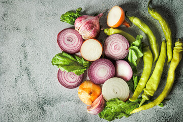 Top view of fresh sliced onions, hot green peppers and greens on light concrete background. Natural light, rustic style, organic autumn harvest, clean eating mood
