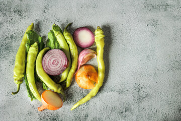 Rustic flat lay of sliced onions, tsitsak peppers, and leafy greens on a concrete background. Natural autumn light, Georgian market vibes, healthy organic produce