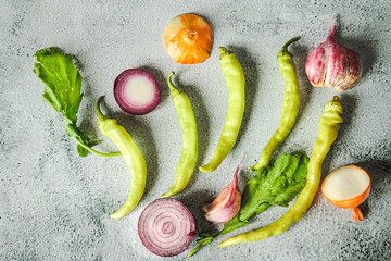 Rustic flat lay of sliced onions, tsitsak peppers, and leafy greens on a concrete background. Natural autumn light, Georgian market vibes, healthy organic produce
