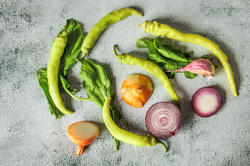 Rustic flat lay of sliced onions, tsitsak peppers, and leafy greens on a concrete background. Natural autumn light, Georgian market vibes, healthy organic produce
