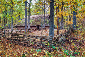Longhouse in the forest in autumn with a fence of branches