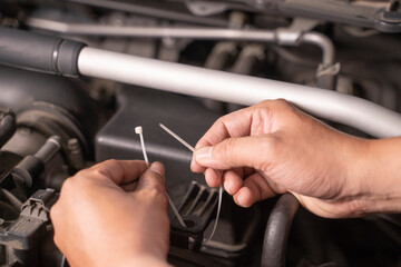 Asian man uses cable ties as temporary replacement nuts for basic car maintenance.