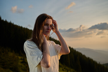 Close-up portrait of a young woman standing on a mountain at sunrise. Peaceful morning in nature,...