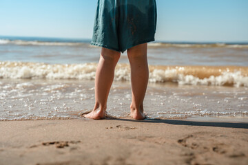 Cute little child girl runs on the sand on the beach and plays with the waves with her bare feet in summer