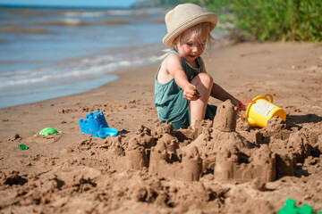 Cute little child girl makes a sand castle with molds on the beach in summer