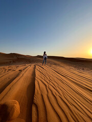 Woman standing on golden desert dunes at sunset in UAE, scenic sand landscape with clear sky, travel and adventure concept