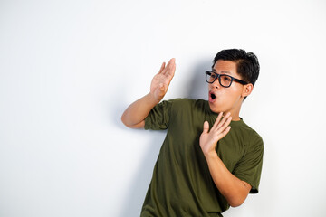 A young Asian man wearing a green t-shirt and glasses shows a surprised expression with hands...