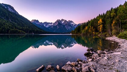 Serene mountain landscape reflects perfectly in the calm lake water under a pastel colored dusk sky. Forest surrounds