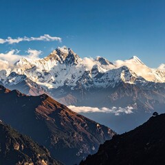 Majestic snow-capped mountain range with hazy valleys, verdant slopes, and scattered clouds under a clear blue sky, bathed in golden sunlight