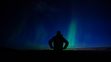 Fototapeta premium Man observing aurora borealis polar lights and Milky Way Stars from a dark countryside location.