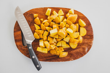 chopped baby potatoes on wooden board with knife on kitchen bench