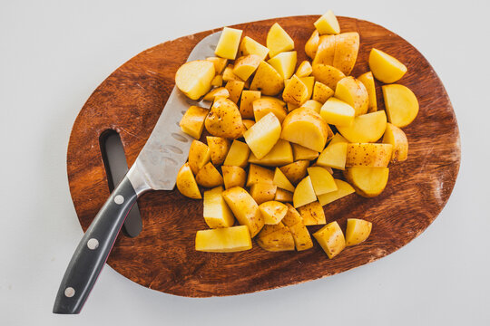 chopped baby potatoes on wooden board with knife on kitchen bench