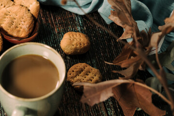 hot drink in blue mug with homemade cookies, dry leaves decoration, fall autumn vibes, rustic cozy seasonal mood
