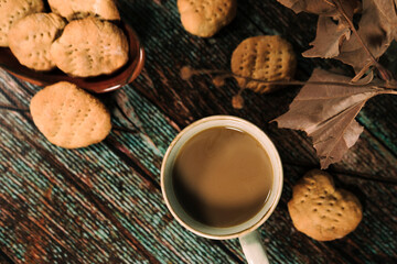 hot drink in blue mug with homemade cookies, heart shaped bisquit, dry leaves decoration, fall autumn vibes, rustic cozy seasonal mood