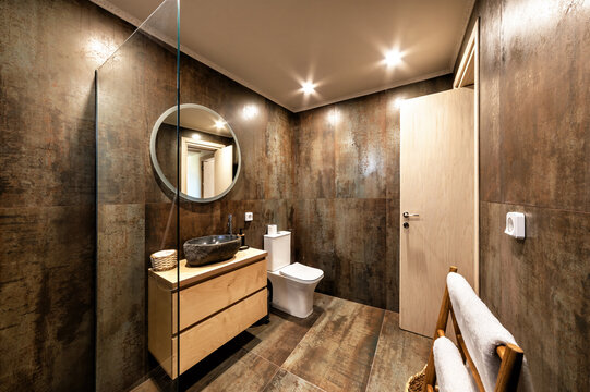 Contemporary bathroom featuring stone basin, sleek toilet, wooden vanity, rustic wall textures, and glass walk-in shower. Interior blends modern comfort, spa-like ambiance, and elegant architectural d