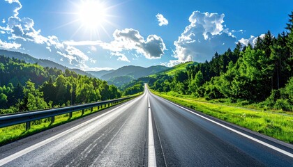 Fototapeta premium A pristine, sun-drenched asphalt road stretches into the distance, framed by lush green mountains and a vibrant blue sky dotted with clouds