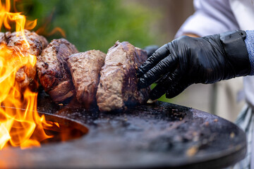 Chef grilling juicy pieces of meat over open flames on a barbecue grill.