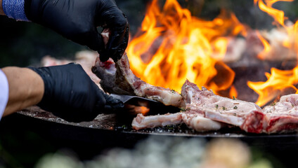 Chef grilling juicy pieces of meat over open flames on a barbecue grill.