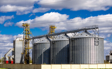 Obraz premium modern granary elevator with silver silos on agro-processing and manufacturing plant for processing drying cleaning and storage of agricultural products, flour, cereals and grain.