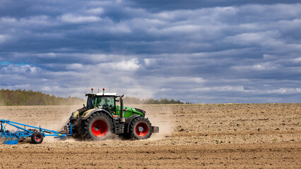 Obraz premium Agriculture machinery in action, a tractor plows a field on a bright day. Farmer in tractor preparing land with seedbed cultivator