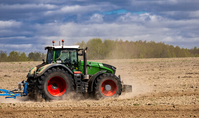 Fototapeta premium Agriculture machinery in action, a tractor plows a field on a bright day. Farmer in tractor preparing land with seedbed cultivator