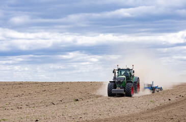 Fototapeta premium A tractor in a field plows the ground at dawn, sowing grain. High quality photo. green tractor plowing cereal field with sky with clouds