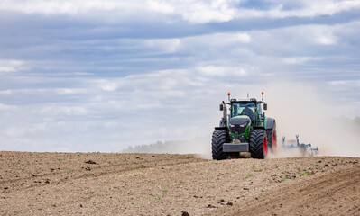 A tractor in a field plows the ground at dawn, sowing grain. High quality photo. green tractor plowing cereal field with sky with clouds