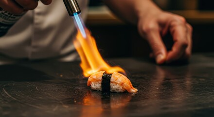 The dynamic moment a sushi chef uses a blowtorch to sear the top of a piece of aburi sushi.