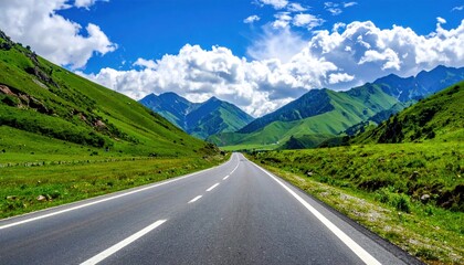 Fototapeta premium Asphalt road stretches into a valley with lush green hills under a bright blue, cloud-filled sky on a clear day