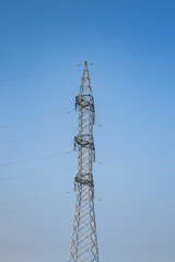 Tall electrical tower stands against clear blue sky with power lines stretching across the horizon