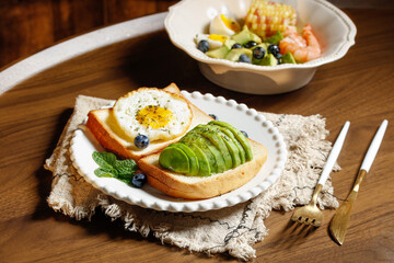 Healthy avocado egg sandwich breakfast with fresh fruit salad on wooden table