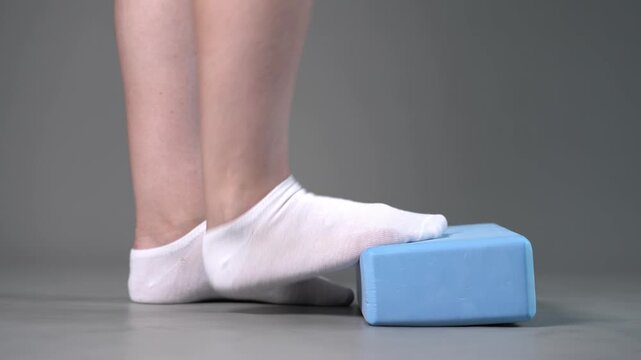 Individual balance training on a blue block with bare feet, demonstrating foot position and stability on a gray studio background