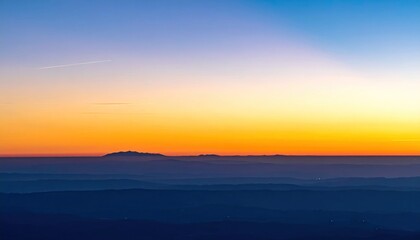Fototapeta premium A vibrant sunset over distant, rolling hills, with deep blues transitioning to orange and yellow hues in the expansive sky