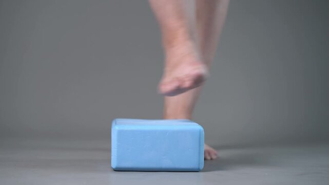 Individual balance training on a blue block with bare feet, demonstrating foot position and stability on a gray studio background