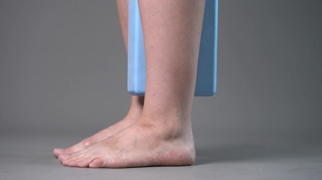 Individual balance training on a blue block with bare feet, demonstrating foot position and stability on a gray studio background