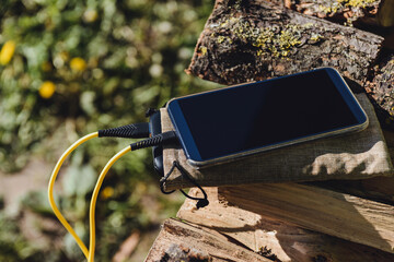 Portable external battery charges a modern smartphone on a pile of firewood, close-up shot.