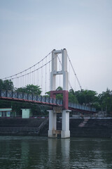 Suspension bridge over river at Mahadev Ghat Raipur,Scenic view of Laxman Jhula bridge with reflection in water,Modern suspension bridge surrounded by greenery in Raipur stock phtoto.