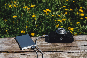 Vintage film camera charging from a modern compact power bank outdoors.