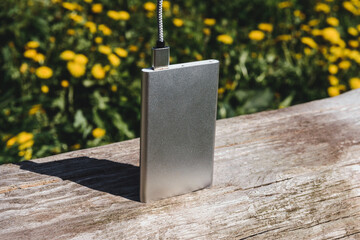 Vertical silver power bank with USB cable on wooden surface outdoors.